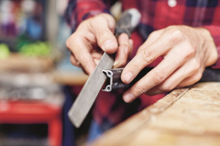 man holding a metal file up against the cut edge of half a bicycle rim